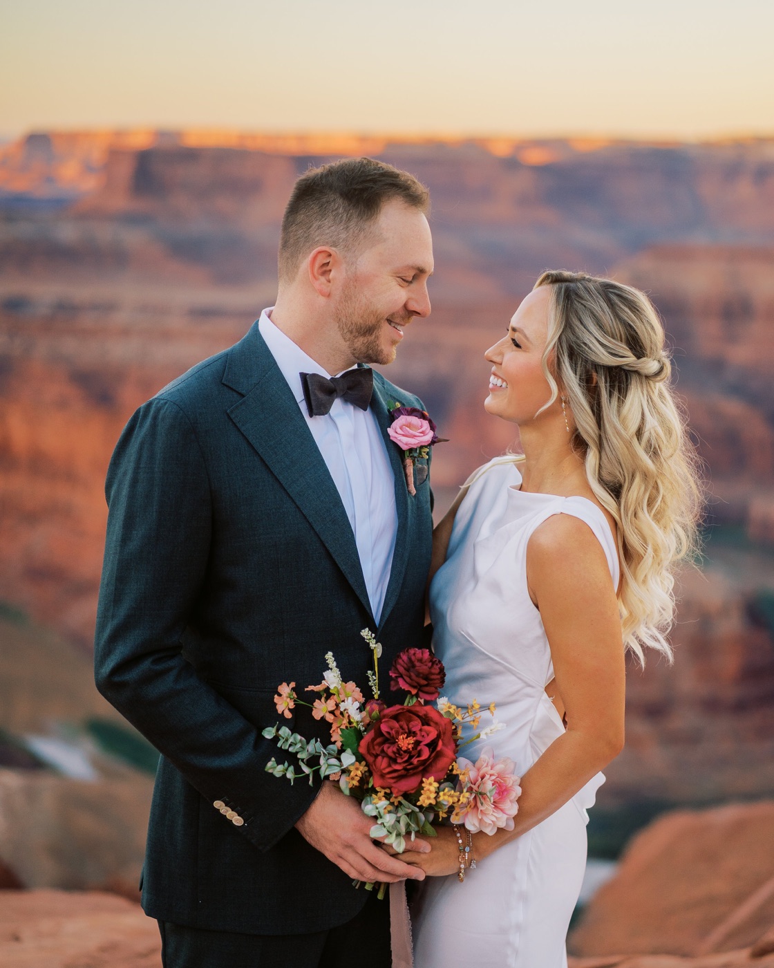 Kacie and Trevor at Dead Horse Point, she holds a bouquet of deep red and peach blooms